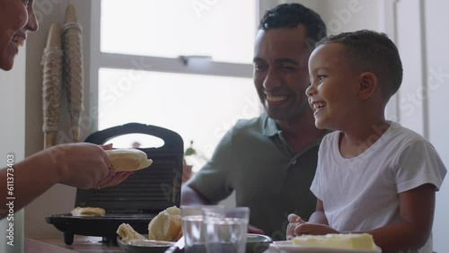Cheerful mixed race family making breakfast while husband and little son eating and drinking juice at kitchen table
