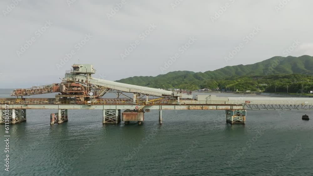 Rusty equipment for loading bulk cargo on pier by green mountainous coast Rusty equipment for loading bulk cargo on pier by green mountainous coast