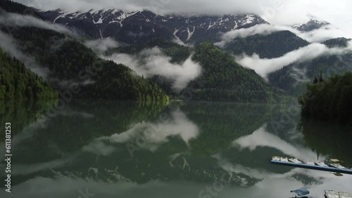 Aerial drone view of lake and green forest in  national Abkhazia park. Clounds lay on mountains. Scenic View of water in a mountain forest lake with pine trees. Lake Ritsa with morning fog photo