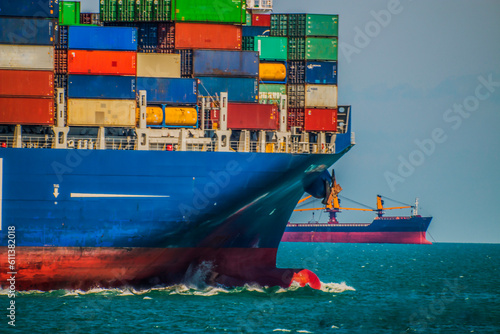 the bow of a large container ship floats against the background of a red-blue ship on the horizon
