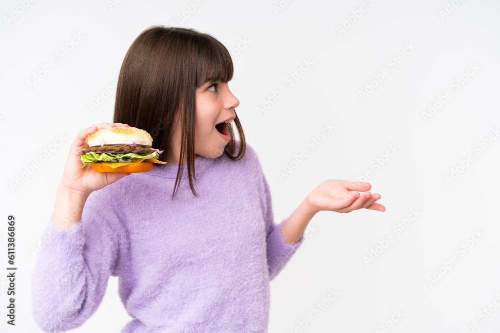 Little caucasian girl holding a burger over isolated background with surprise facial expression Little caucasian girl holding a burger over isolated background with surprise facial expression