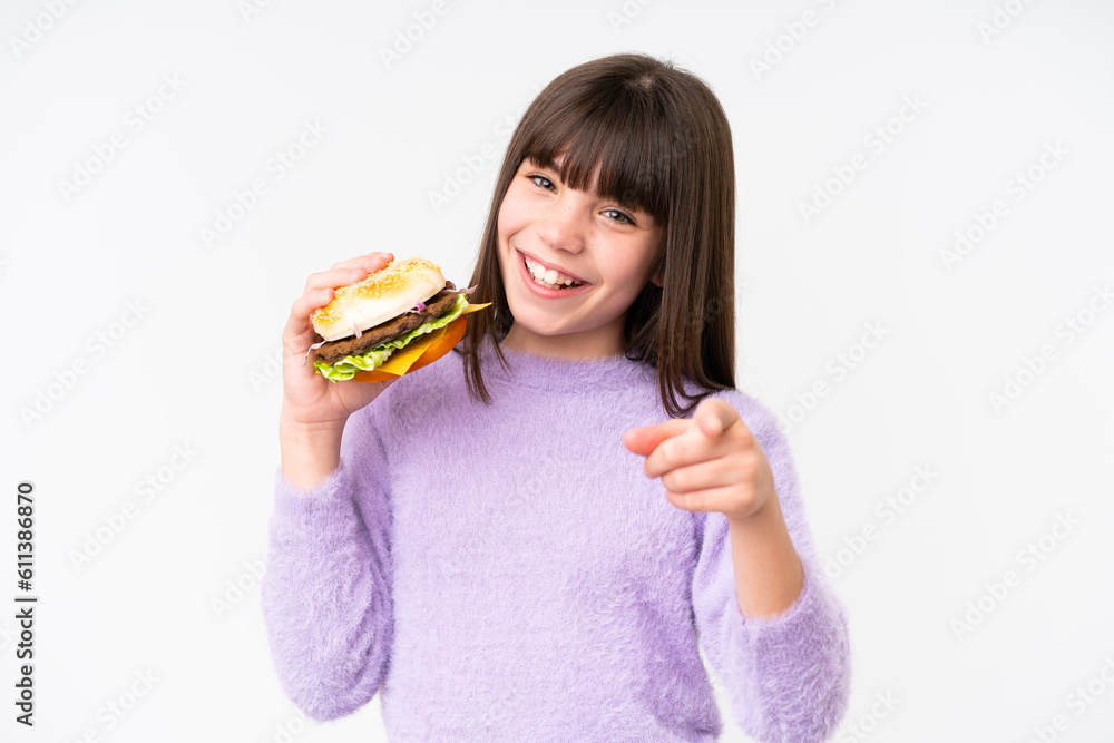 Little caucasian girl holding a burger over isolated background points finger at you with a confident expression Little caucasian girl holding a burger over isolated background points finger at you with a confident expression