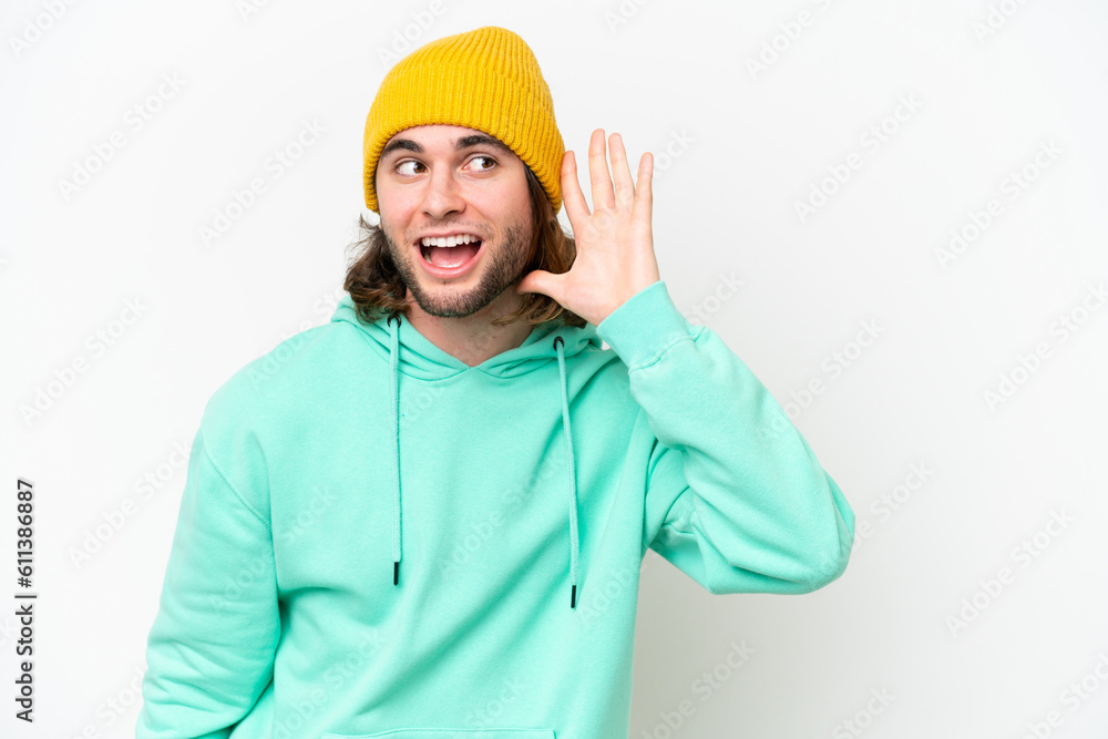 Young handsome man isolated on white chroma background listening to something by putting hand on the ear