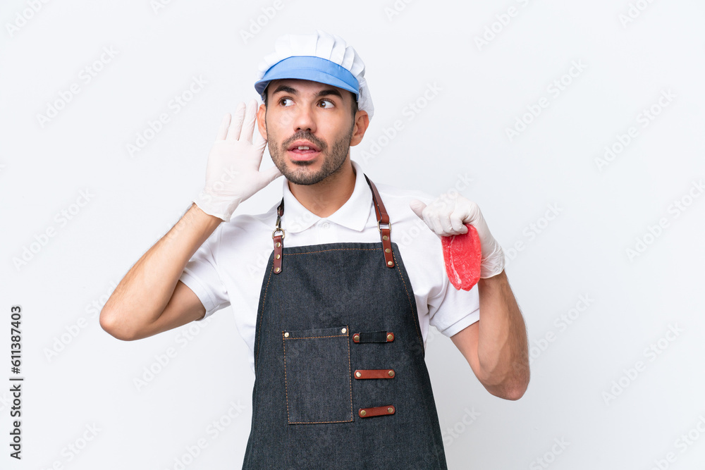 Butcher caucasian man wearing an apron and serving fresh cut meat over isolated white background listening to something by putting hand on the ear Butcher caucasian man wearing an apron and serving fresh cut meat over isolated white background listening to something by putting hand on the ear