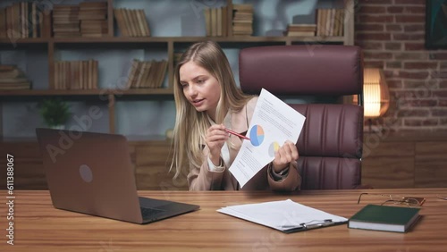 Annoyed female boss dismissing employees for bad underperformance during video conference on wireless laptop. Disappointed lady pointing with pencil on financial indexes while sitting in comfy office photo