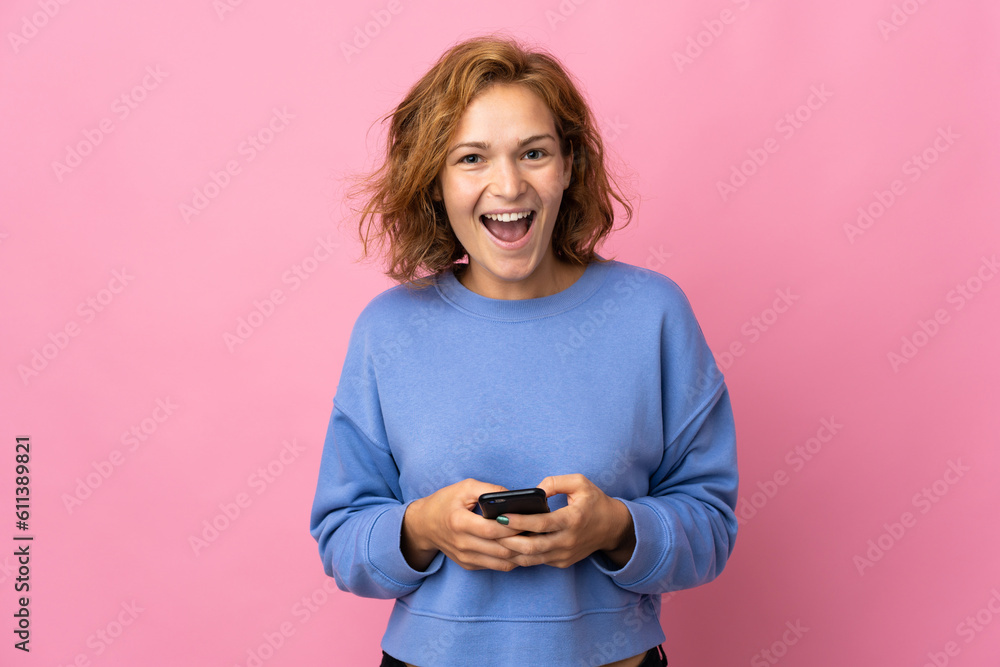 Young Georgian woman isolated on pink background surprised and sending a message Young Georgian woman isolated on pink background surprised and sending a message