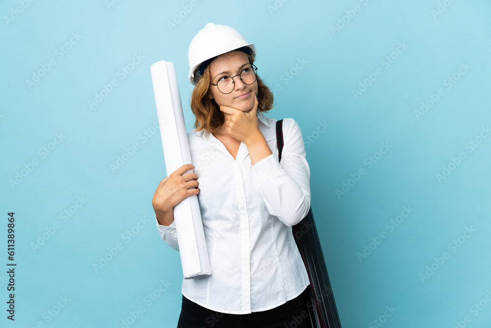 Young architect Georgian woman with helmet and holding blueprints over isolated background having doubts Young architect Georgian woman with helmet and holding blueprints over isolated background having doubts