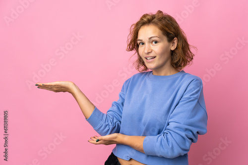 Young Georgian woman isolated on pink background extending hands to the side for inviting to come