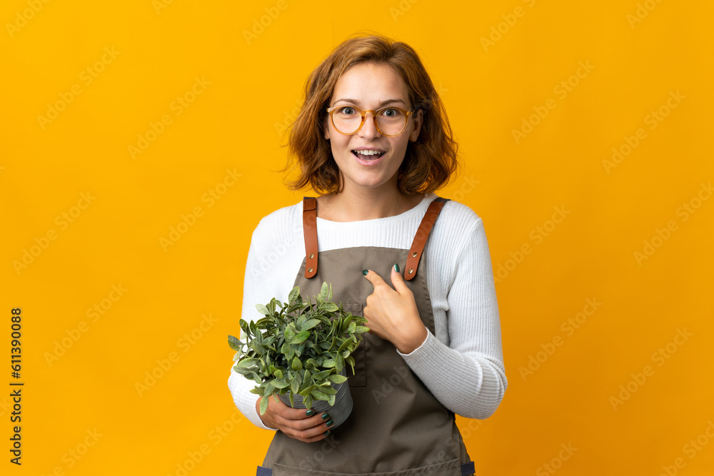 Young Georgian woman holding a plant isolated on yellow background with surprise facial expression Young Georgian woman holding a plant isolated on yellow background with surprise facial expression