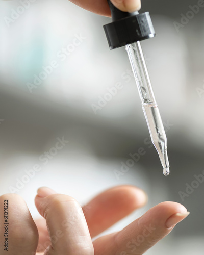 pipette in woman's hand. woman drips clear liquid onto her finger. Gray light background. Close-up. Side view. Copy space. Soft focus. 