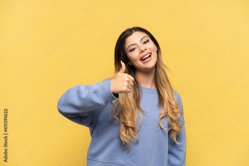 Young Russian girl isolated on yellow background with thumbs up because something good has happened Young Russian girl isolated on yellow background with thumbs up because something good has happened