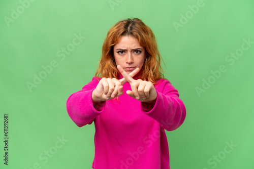 Young caucasian woman isolated on green screen chroma key background making stop gesture with her hand to stop an act