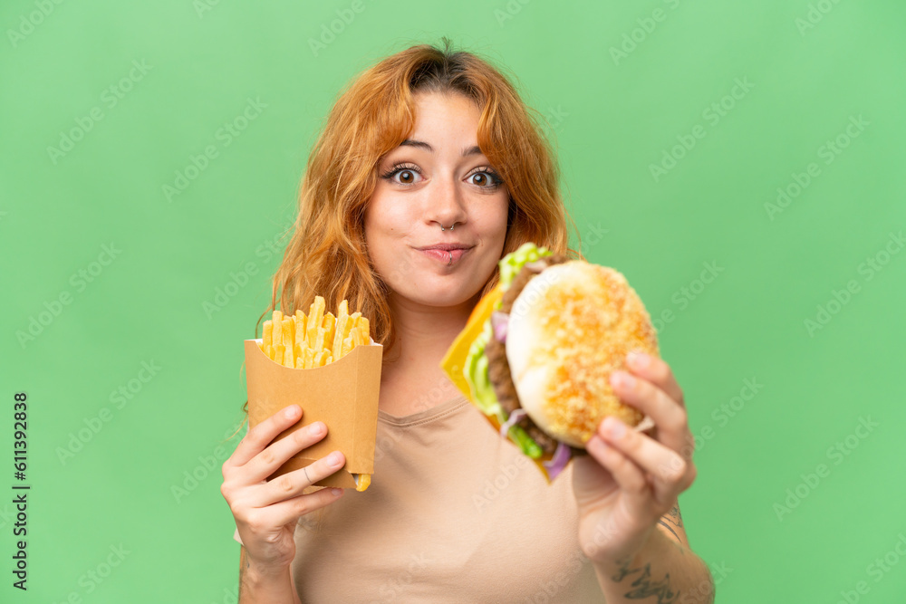 Young caucasian woman holding fried chips and burger isolated on green screen chroma key background Young caucasian woman holding fried chips and burger isolated on green screen chroma key background