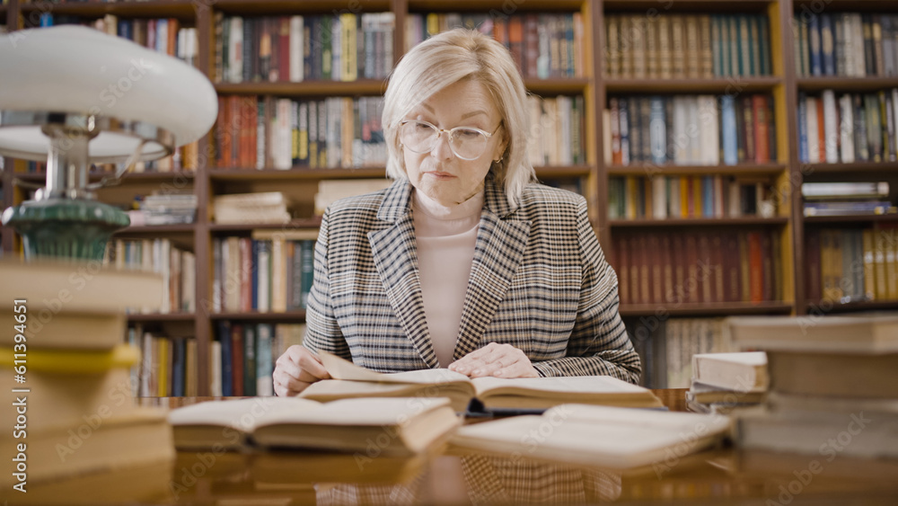 Senior woman reading a book in the library, writer doing research, comfortable workplace Senior woman reading a book in the library, writer doing research, comfortable workplace
