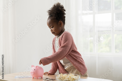 Girl kid putting money into the piggybank. African American girl kid inserting a coin in a piggy bank. Kid investment for future concept photo