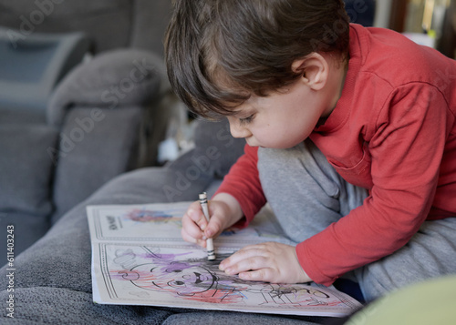 young boy drawing in the coloring book on the couch