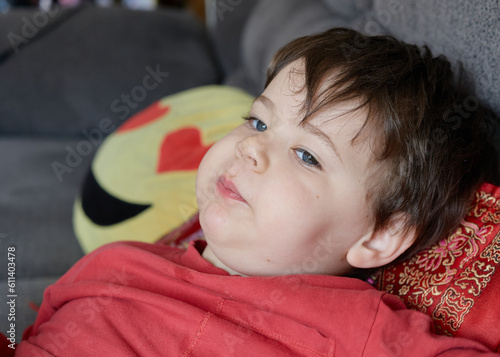 cute expressive young boy lounging on the couch and eating an apple at home photo