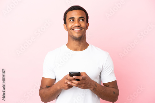 African American handsome man on isolated pink background using mobile phone and looking up © luismolinero