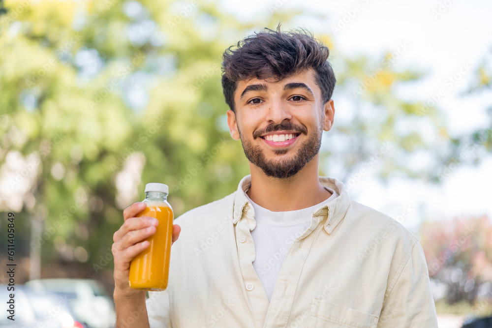 Fototapeta premium Young Arabian handsome man holding an orange juice at outdoors smiling a lot