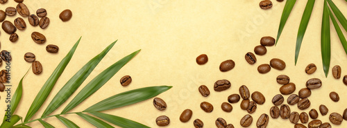 Coffee banner suitable for caffeine and coffee producers. Flat lay with natural coffee beans and palm leaves on a craft paper with copy space. Harvest coffee. Banner size, copy space