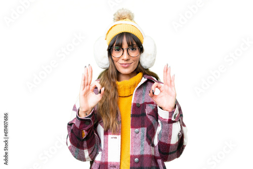 Young caucasian woman wearing winter muffs over isolated chroma key background showing an ok sign with fingers