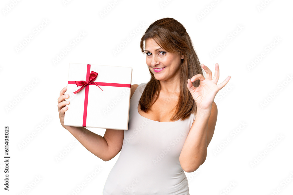 Middle age caucasian woman holding a gift over isolated background showing ok sign with fingers Middle age caucasian woman holding a gift over isolated background showing ok sign with fingers