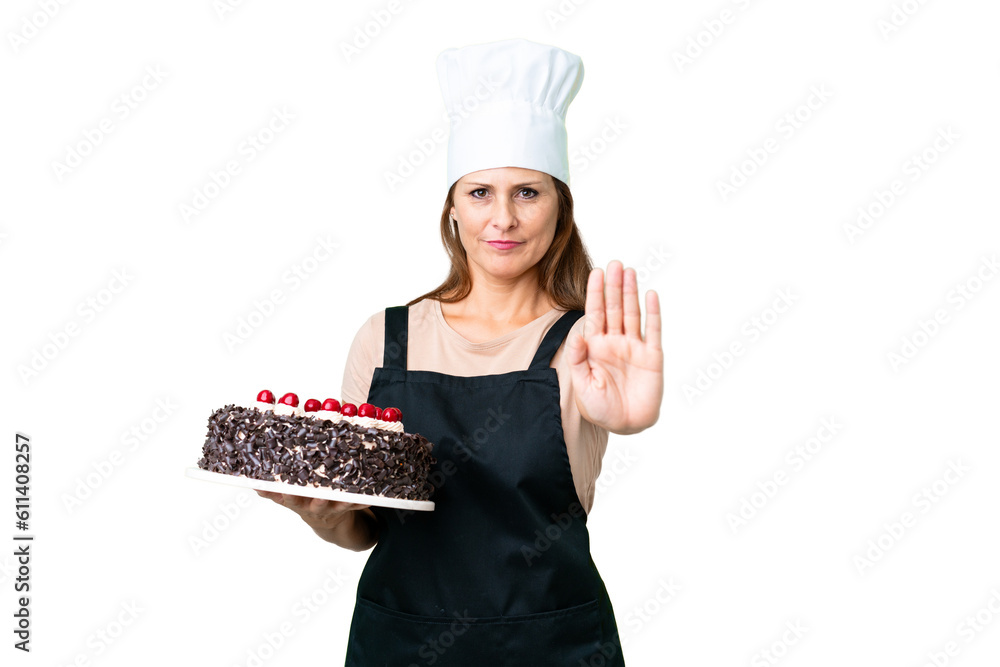 Middle age pastry chef woman holding a big cake over isolated background making stop gesture Middle age pastry chef woman holding a big cake over isolated background making stop gesture
