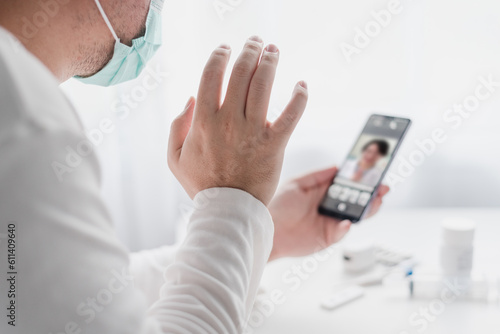 telemedicine and home health care concept  a man wearing a mask and holding a smart phone in their hand and conference with doctor on the screen.
