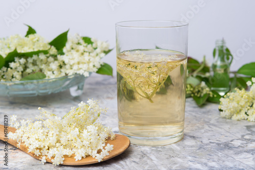 Homemade elderflower drink with sugar and lemon in a glass, light background