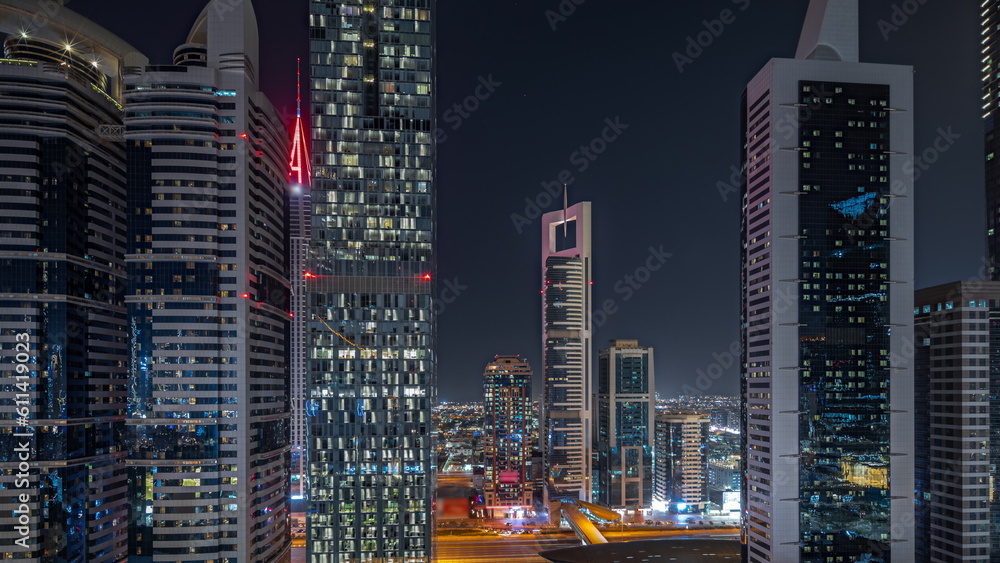 Panorama showing aerial view of Dubai International Financial District with many skyscrapers night timelapse.