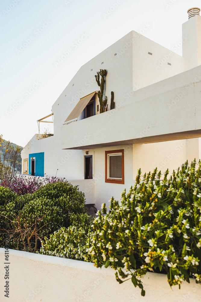 Fototapeta premium Front view of white facade of beach holiday apartment building. White and blue facade with trees and cactus with sunset light.