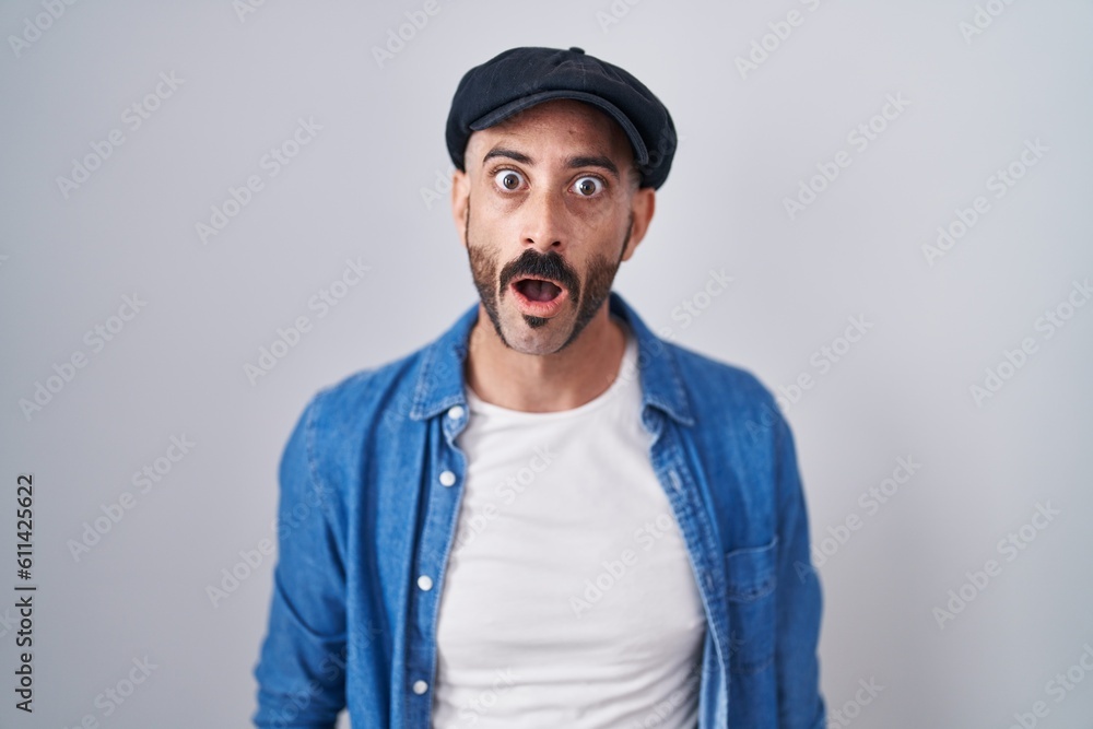 Hispanic man with beard standing over isolated background in shock face, looking skeptical and sarcastic, surprised with open mouth Hispanic man with beard standing over isolated background in shock face, looking skeptical and sarcastic, surprised with open mouth