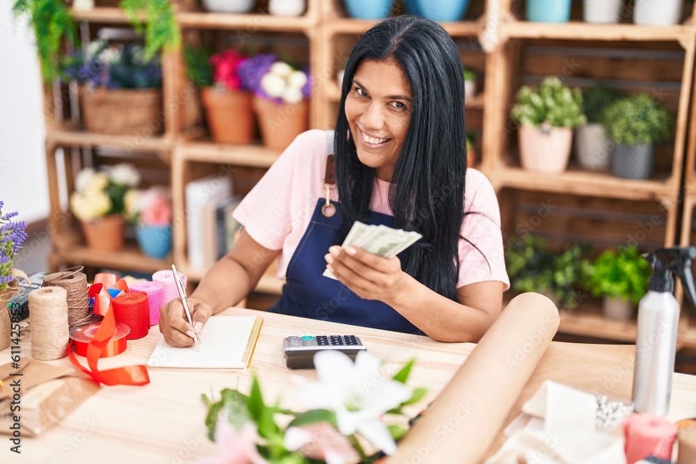 Fototapeta premium Middle age hispanic woman florist counting dollars writing on notebook at florist