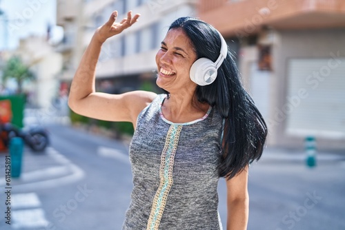 Middle age hispanic woman listening to music and dancing at street