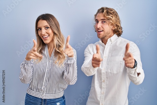 Young couple standing over blue background pointing fingers to camera with happy and funny face. good energy and vibes.