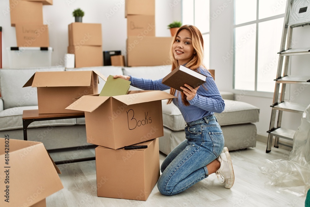 Young caucasian woman smiling confident putting books on cardboard box at new home Young caucasian woman smiling confident putting books on cardboard box at new home