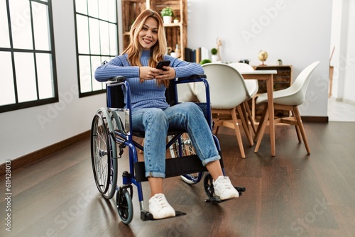 Young caucasian woman using smartphone sitting on wheelchair at home © Krakenimages.com