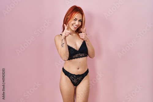 Young caucasian woman wearing lingerie over pink background pointing fingers to camera with happy and funny face. good energy and vibes.