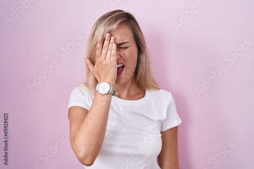 Young blonde woman standing over pink background yawning tired covering half face  eye and mouth with hand. face hurts in pain.