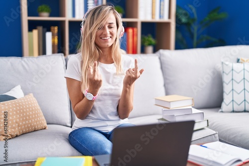 Young blonde woman studying using computer laptop at home showing middle finger doing fuck you bad expression, provocation and rude attitude. screaming excited