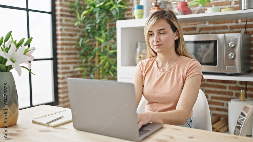 Young blonde woman using laptop sitting on table at dinning room Young blonde woman using laptop sitting on table at dinning room