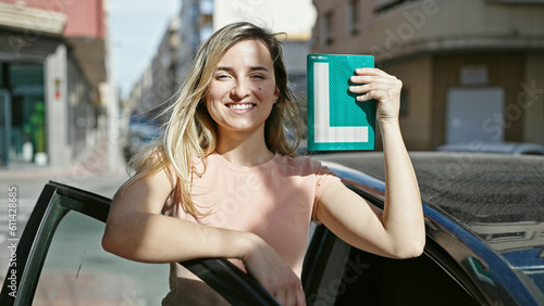 Fotografie Young blonde woman smiling confident holding new driver license at street