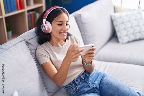 Young beautiful hispanic woman playing video game sitting on sofa at home