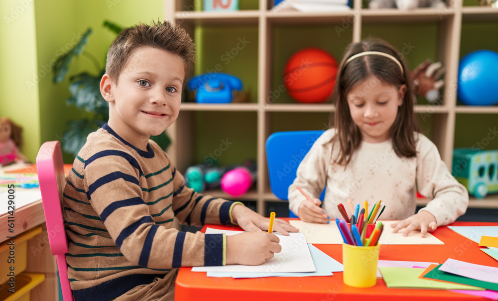 Fototapeta premium Adorable boy and girl preschool students sitting on table drawing on paper at kindergarten
