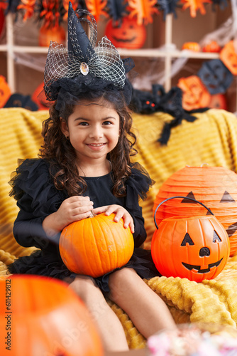 Adorable hispanic girl having halloween party holding pumpkin at home