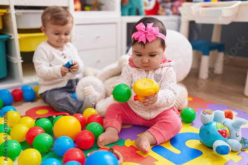 Adorable boy and girl playing with balls sitting on floor at kindergarten