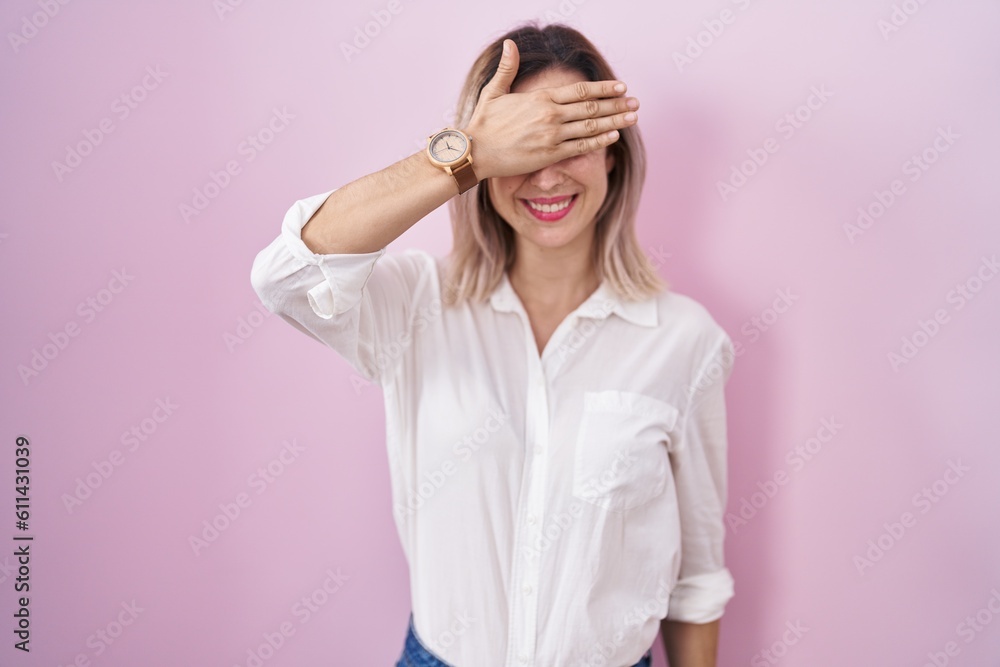Young beautiful woman standing over pink background smiling and laughing with hand on face covering eyes for surprise. blind concept. Young beautiful woman standing over pink background smiling and laughing with hand on face covering eyes for surprise. blind concept.