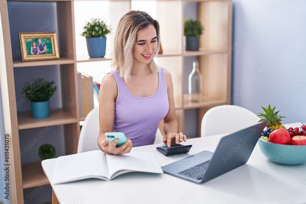 Young woman using smartphone and calculator studying at home