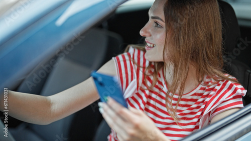 Young blonde woman using smartphone driving car at street