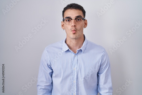 Handsome hispanic man wearing business clothes and glasses making fish face with lips, crazy and comical gesture. funny expression.